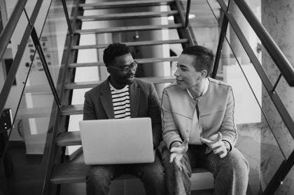 Young African American business man and short hair woman working on laptop while sitting at office stairs